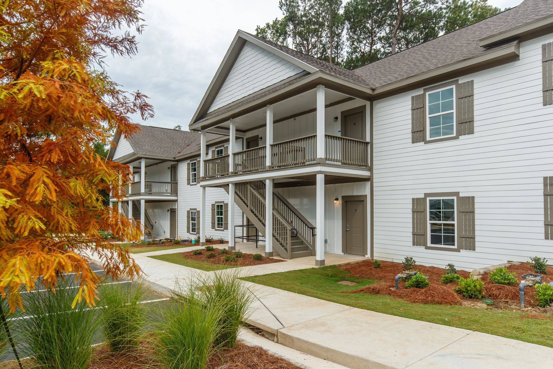 Apartment building exterior with white siding, covered porch, and autumn trees