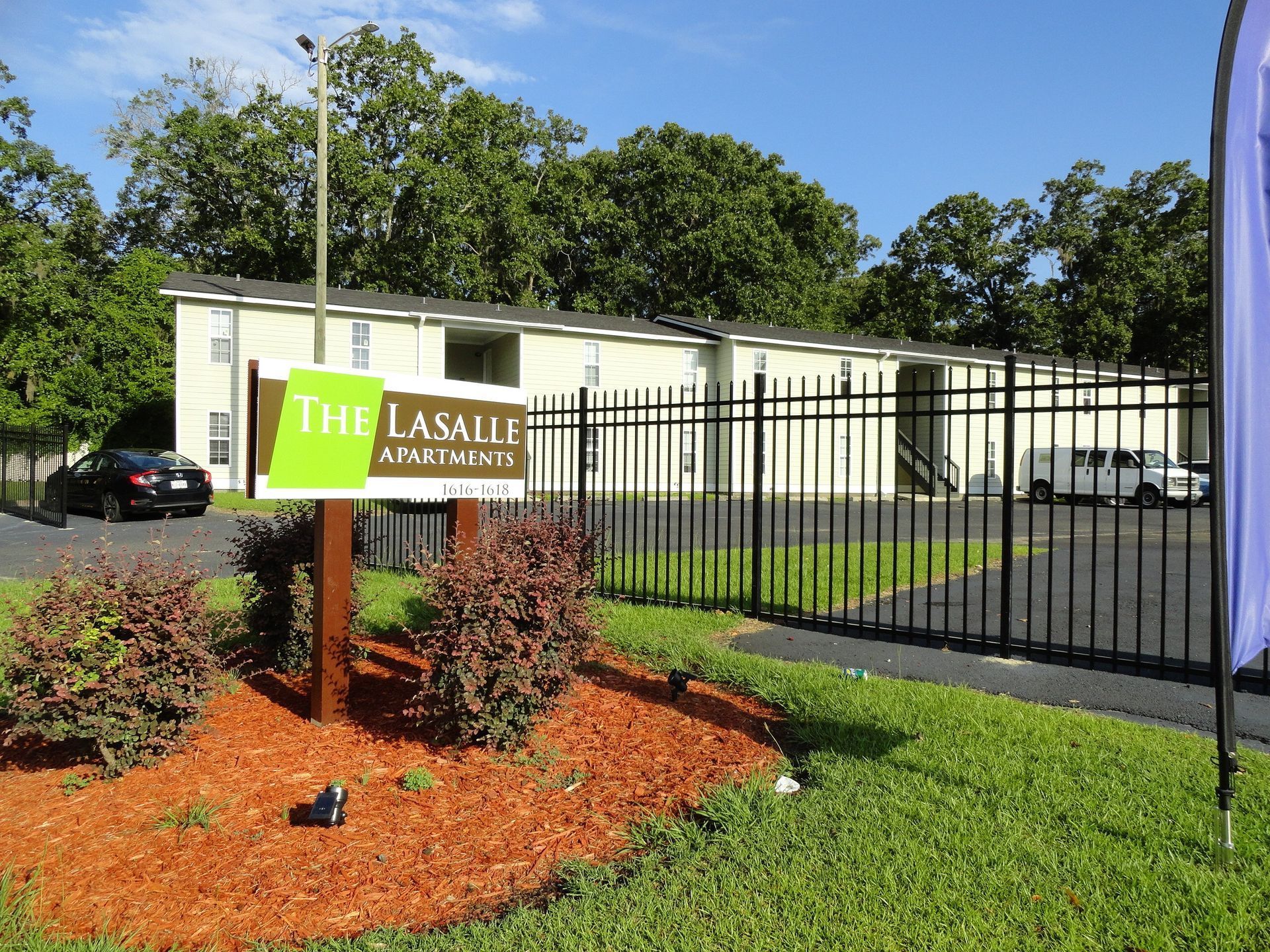 The LaSalle Apartments sign by a black fence and parked cars on a sunny day