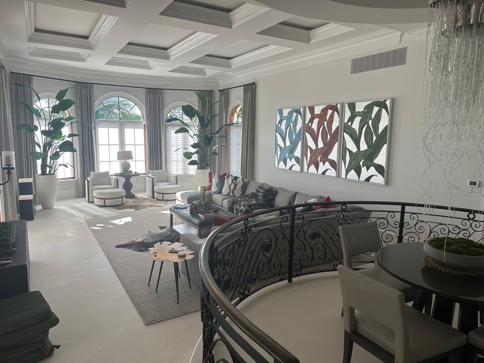 Spacious living room with large windows, artwork, and a wrought-iron balcony overlooking a dining area.