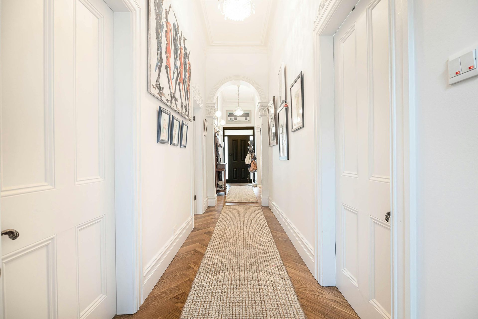Long hallway with white walls and doors, wooden floor, and a patterned rug.