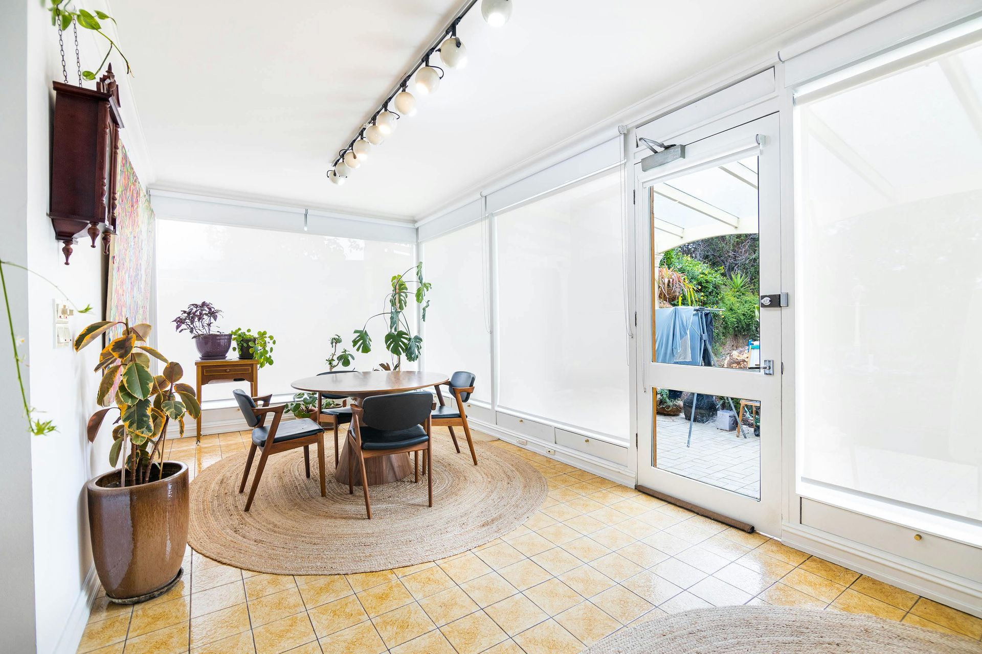 Bright sunroom with a table and chairs, plants, and a door to an outdoor area.