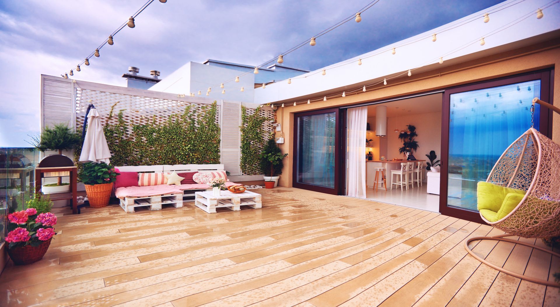 Rooftop patio with wooden deck, sliding doors to an interior space, a hanging chair, and string lights.