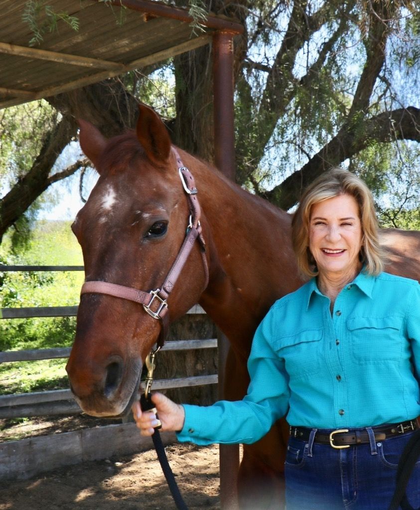 Woman in turquoise shirt with a brown horse in a ranch setting, smiling.