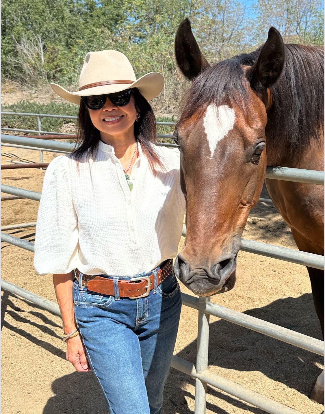 Arlene I Woman in cowboy hat smiles next to a brown horse with a heart-shaped marking on its forehead.