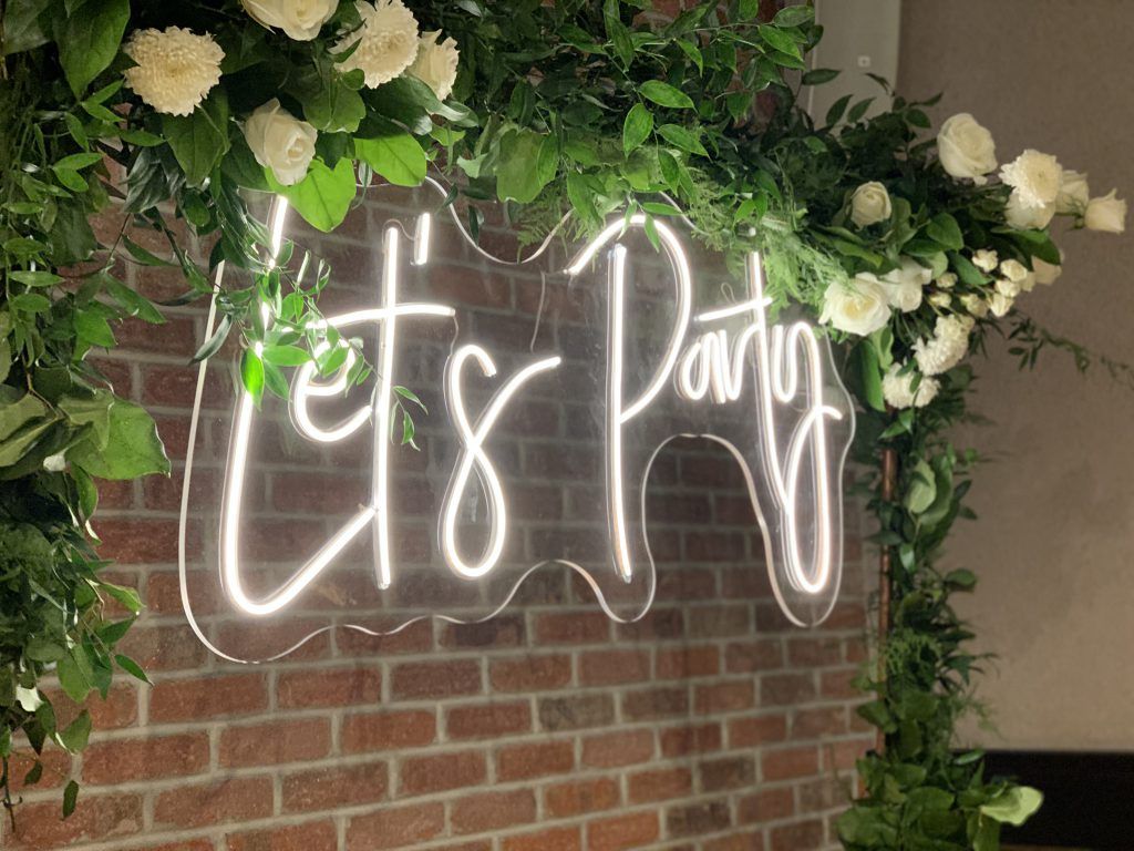 A neon sign that says `` let 's party '' is hanging on a brick wall.