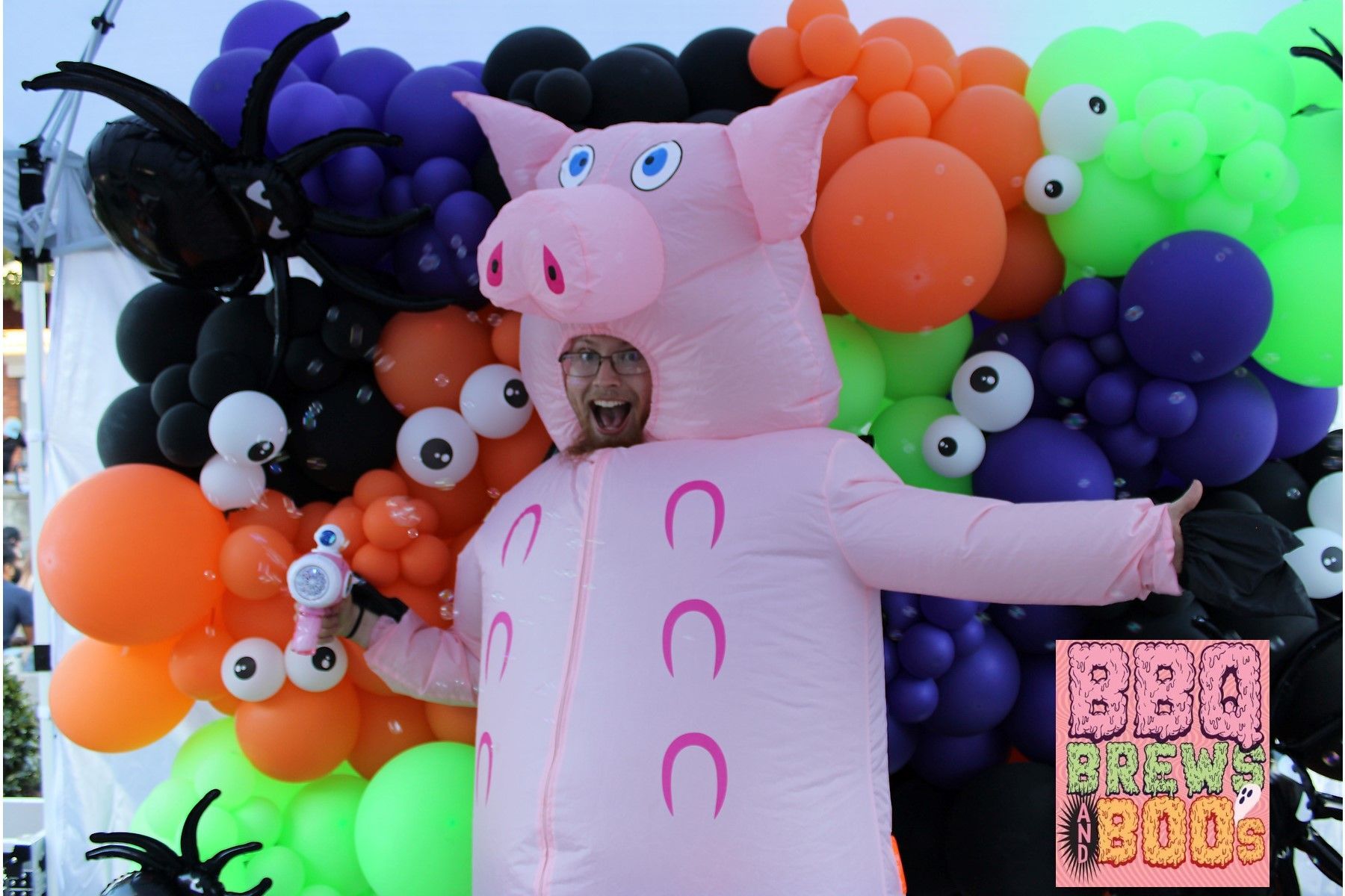 A man in an inflatable pig costume stands in front of balloons