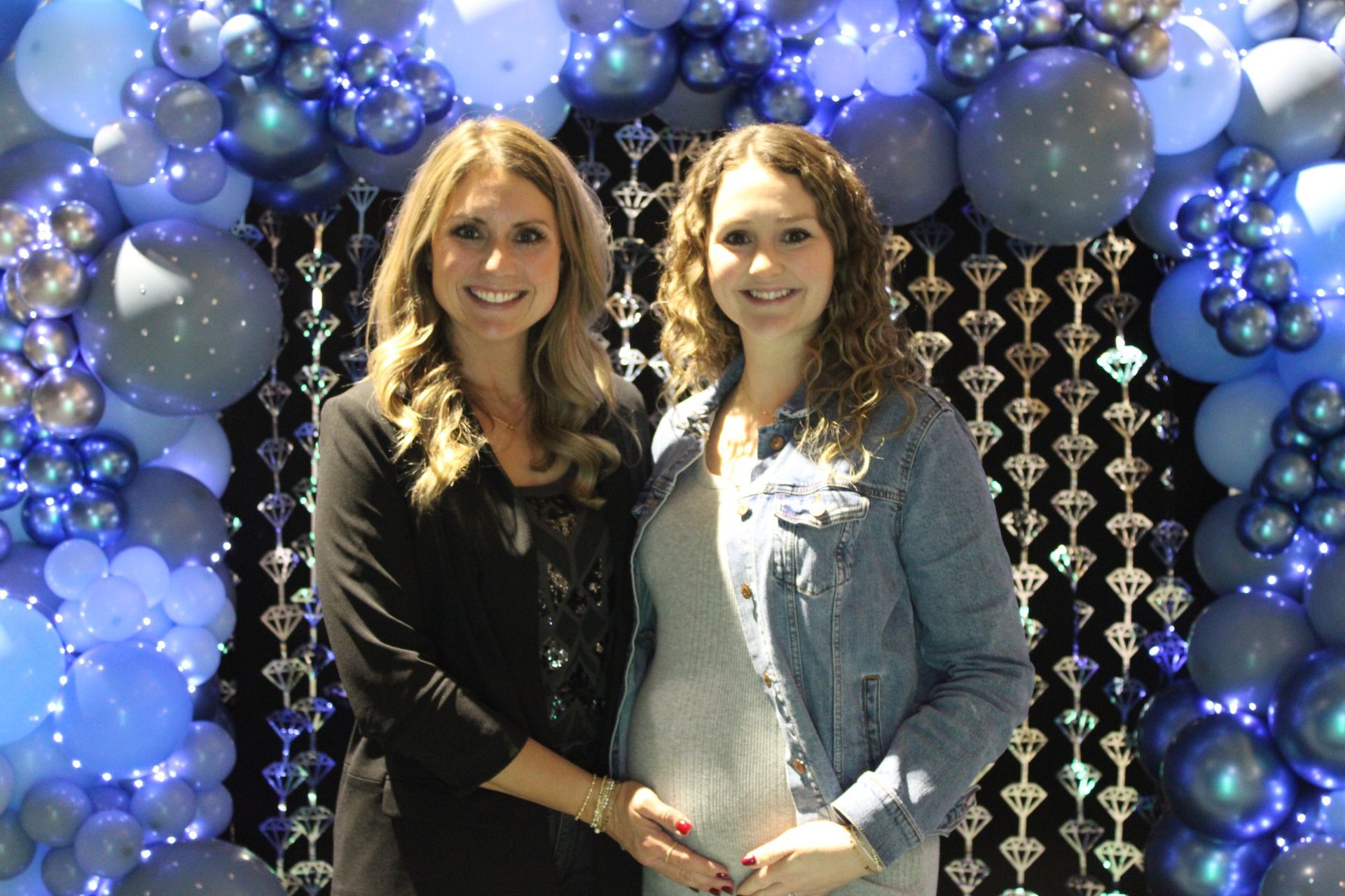 Two women are posing for a picture in front of a wall of balloons.