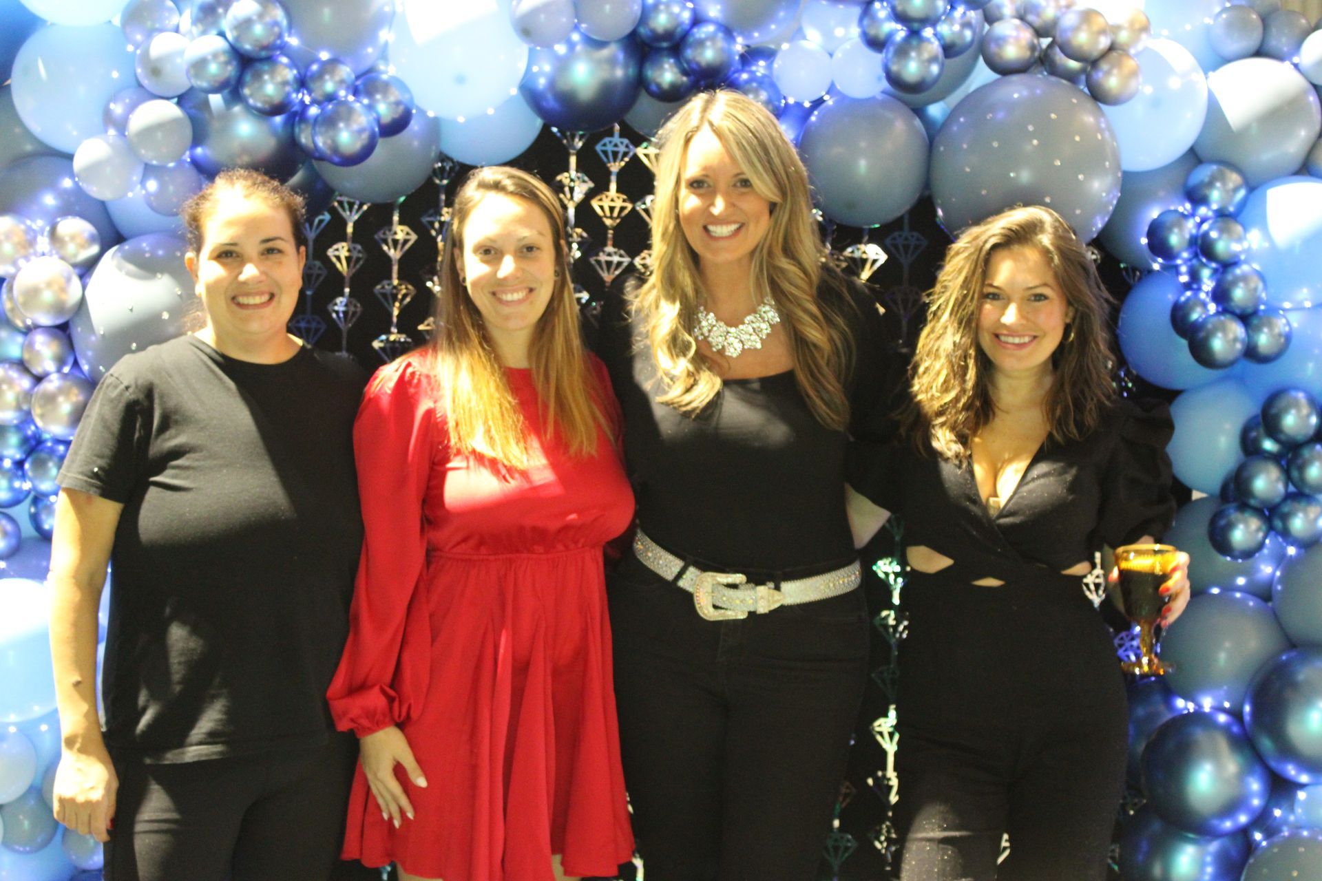 A group of women are posing for a picture in front of a wall of balloons.