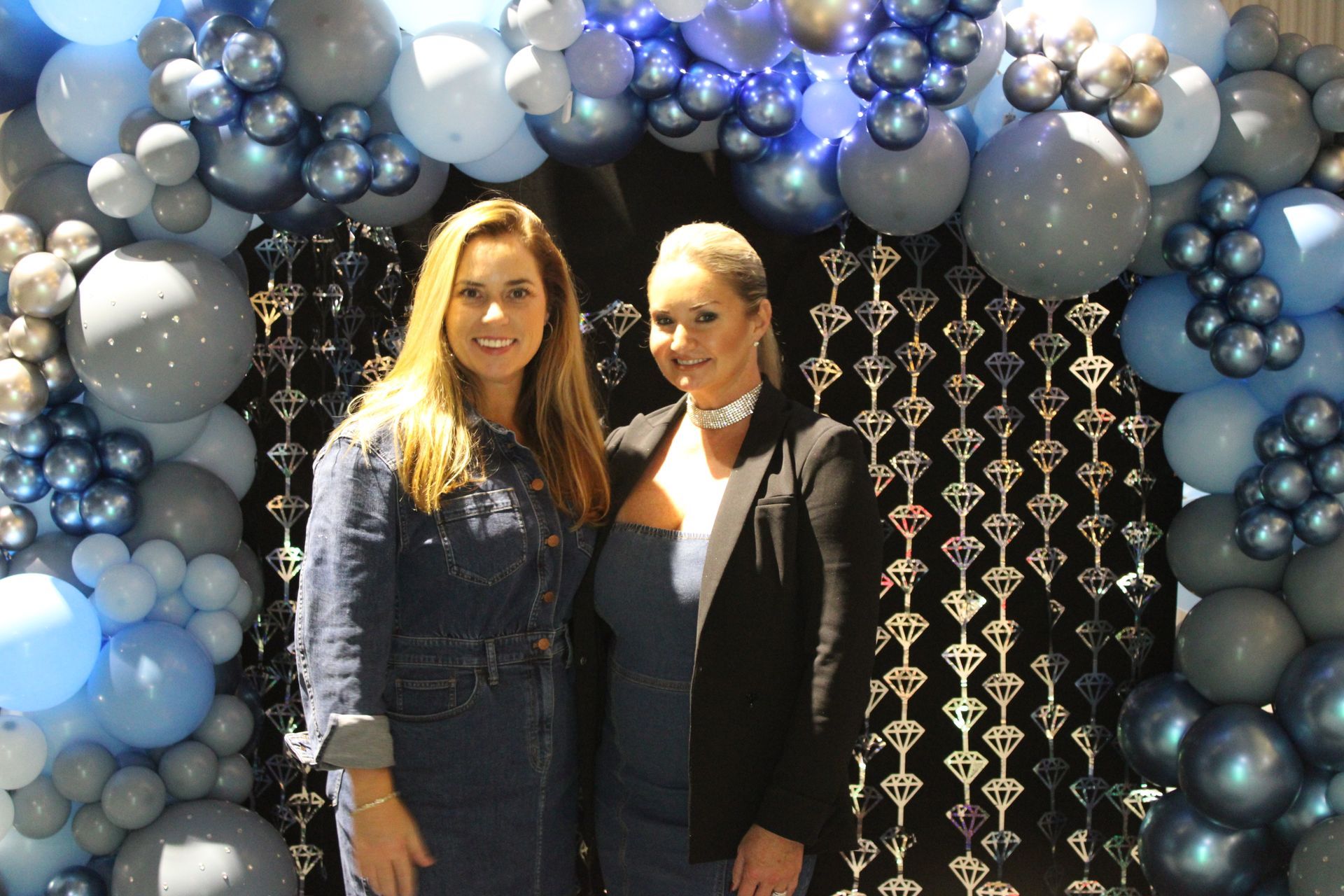 Two women are standing in front of a balloon arch.