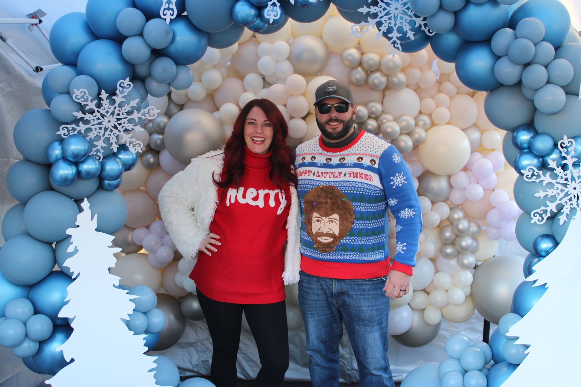 A man and a woman are posing for a picture in front of a wall of balloons.