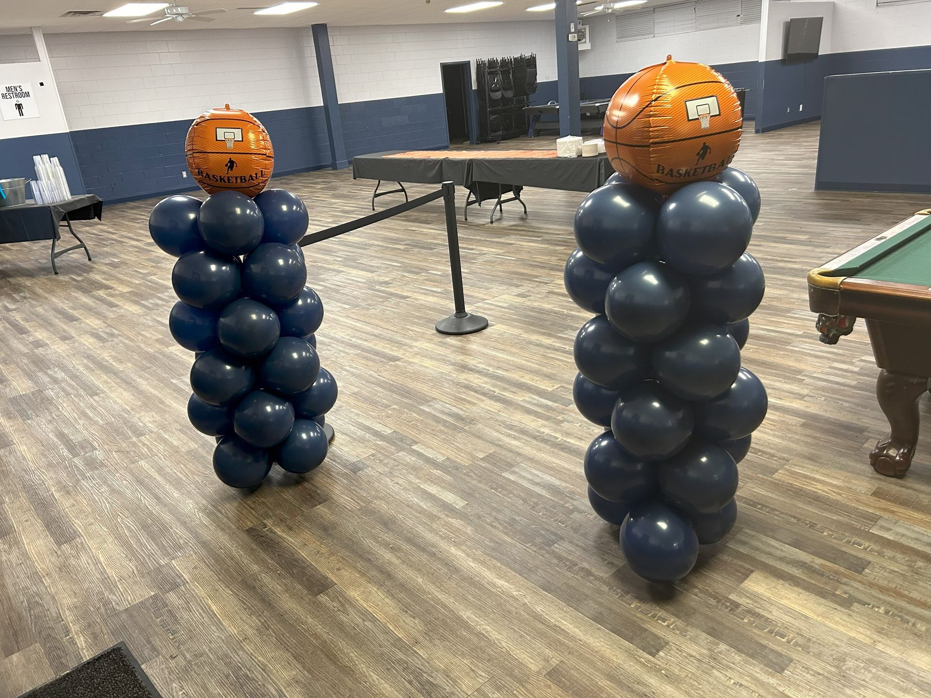 Two columns made of balloons and basketballs in a room with a pool table.