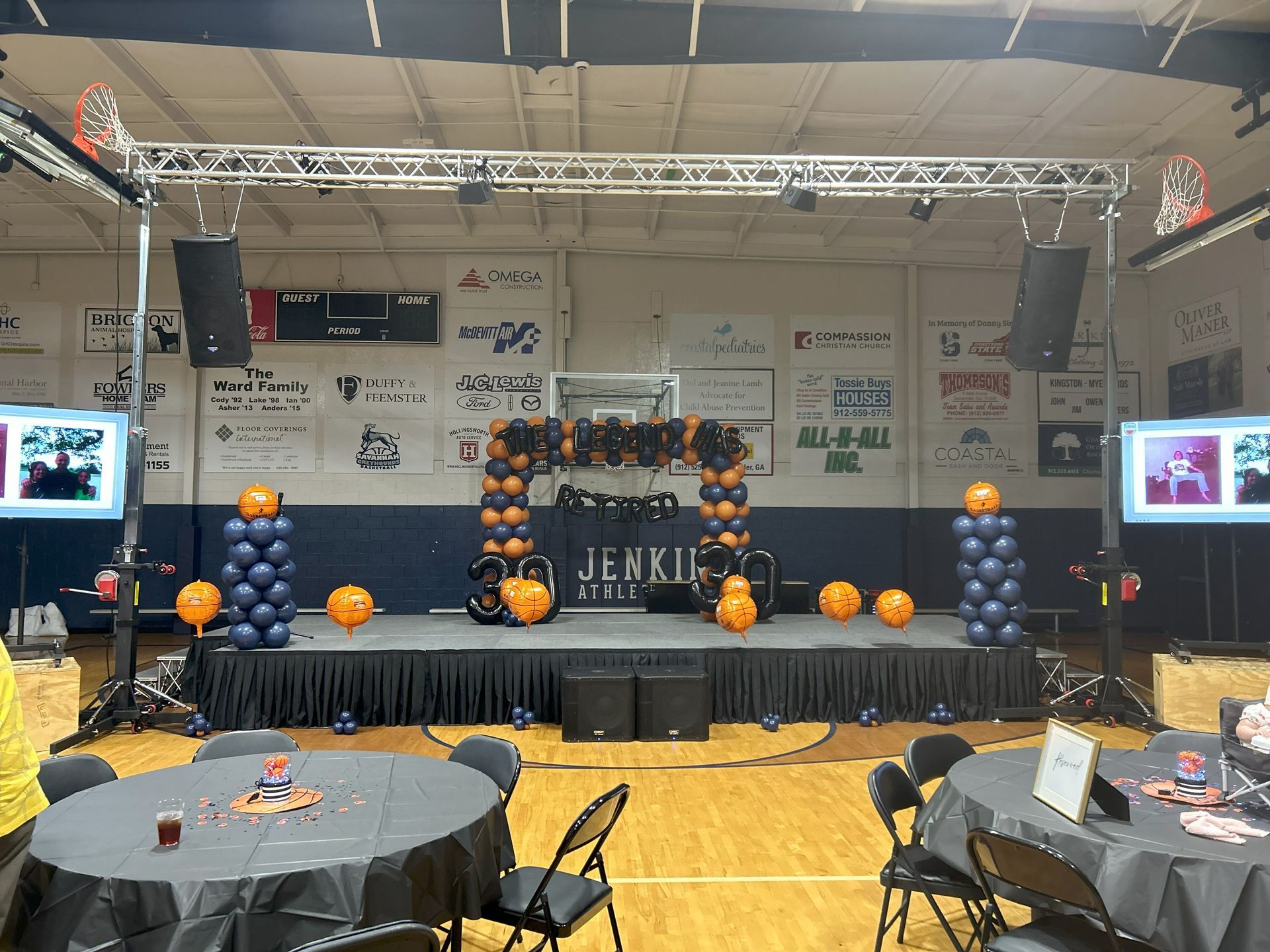 A large room with tables and chairs and balloons on the stage.
