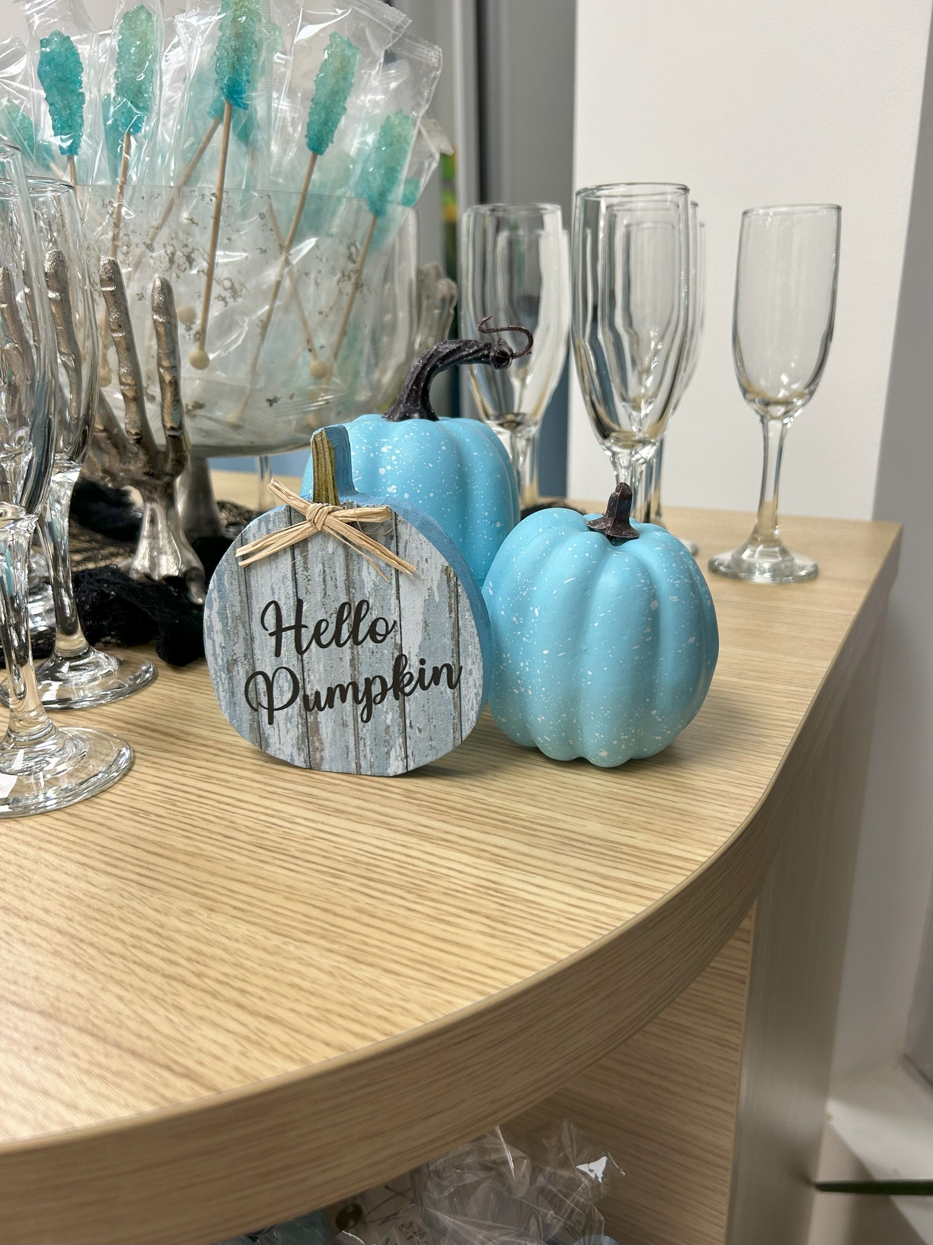 Three blue pumpkins are sitting on a wooden table next to wine glasses.