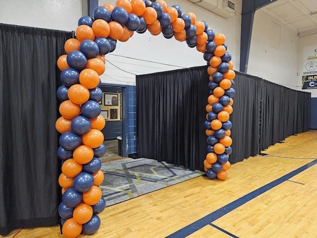 A large arch made of orange and blue balloons in a gym.