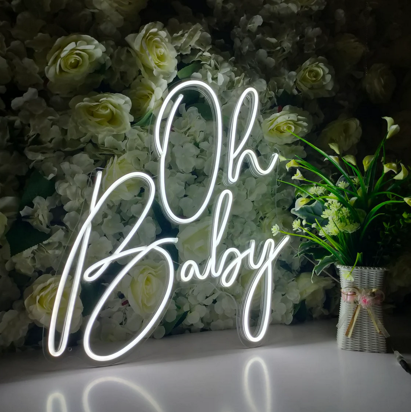 A neon sign that says `` oh baby '' is sitting in front of a wall of flowers.