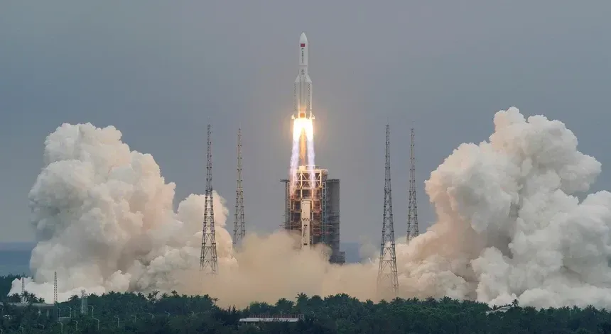 Um grande foguete branco é lançado de uma plataforma de lançamento, cercado por enormes colunas de fumaça contra um céu nublado.