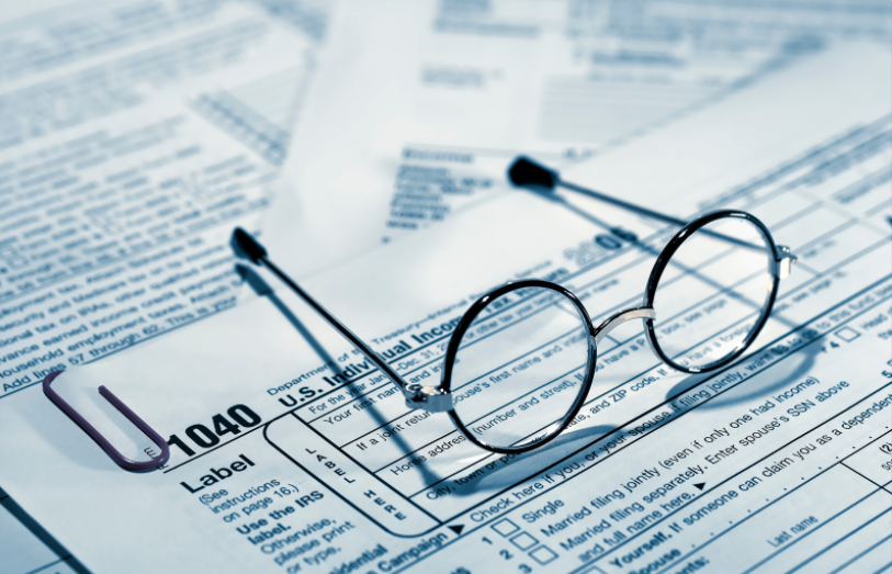 Um par de óculos redondos repousa sobre um formulário de imposto de renda federal americano (formulário 1040), com um clipe de papel roxo próximo a ele.