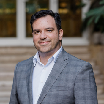 Dr. Nuno BravoUma pessoa de cabelos escuros e barba rala, vestindo um blazer cinza e uma camisa branca de botões, sorri em uma foto de rosto.