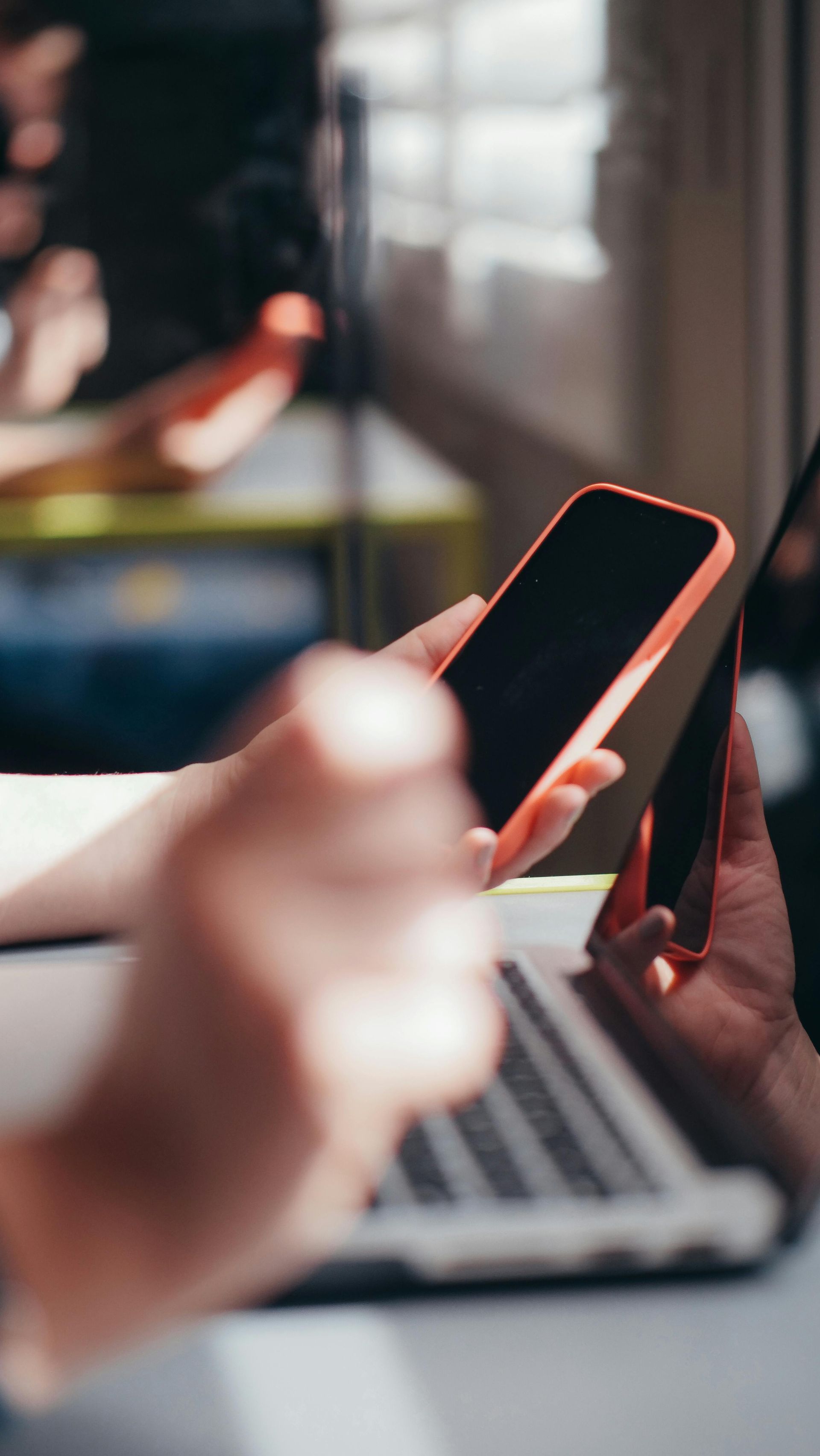 Uma pessoa segura dois smartphones sobre um laptop aberto em um ambiente profissional com iluminação suave.