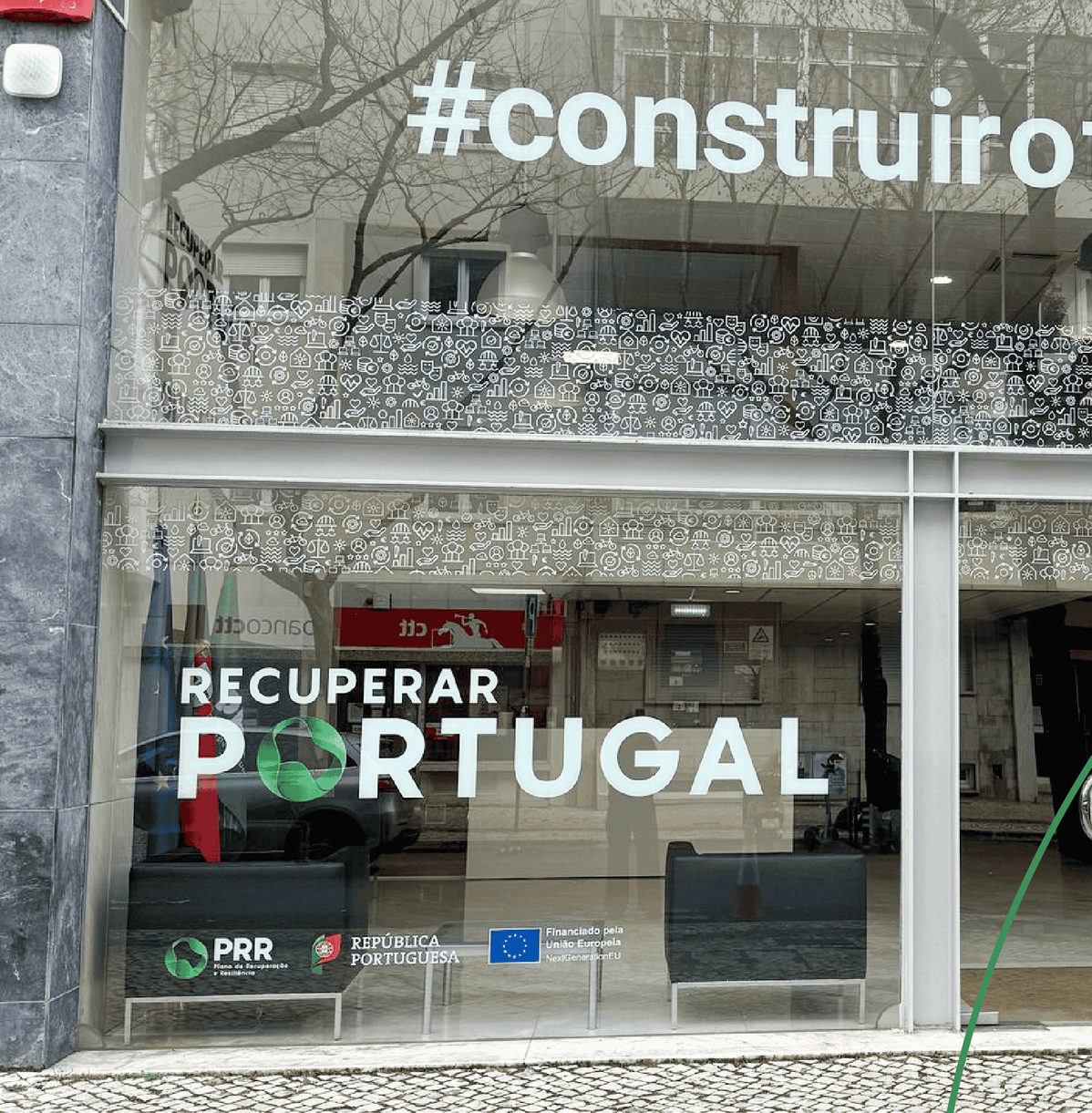 Fachada de vidro com o logotipo “Recuperar Portugal”, a marca PRR e o emblema da União Europeia.