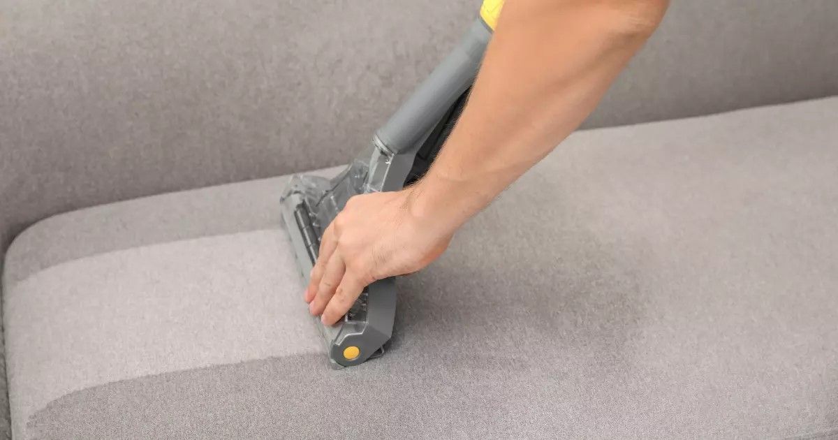 Vacuum nozzle acting as an upholstery cleaner on a light-colored sofa cushion.