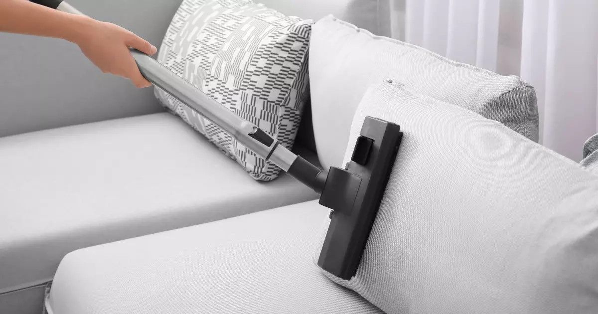 Person using an upholstery cleaner on a gray couch to remove dirt and stains.