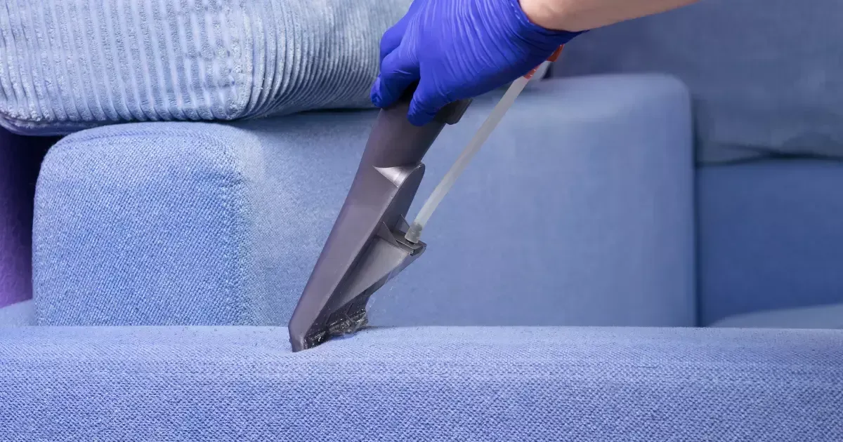 A person using a vacuum cleaner on blue sofa