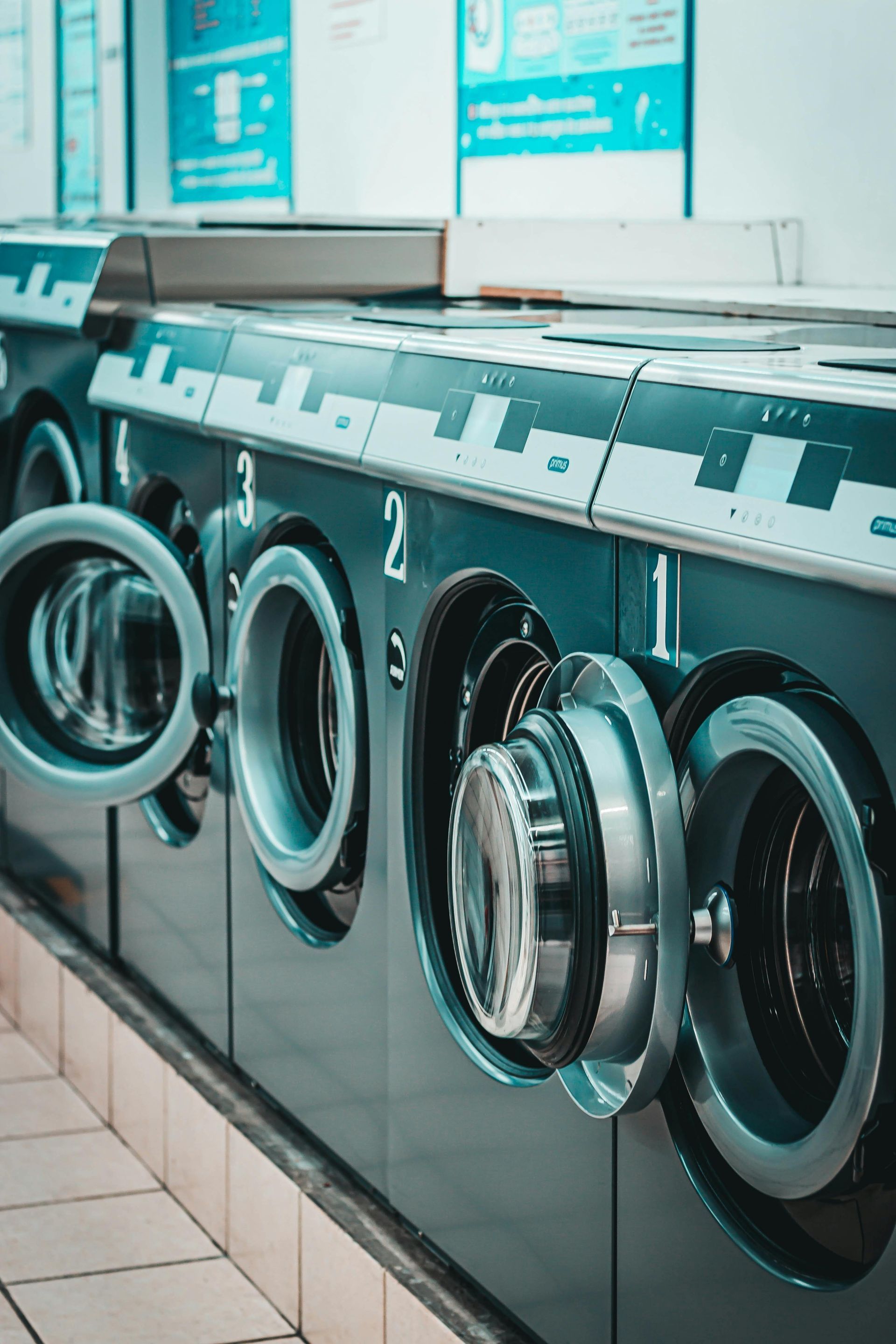 Row of black washing machines with open doors in a laundromat.