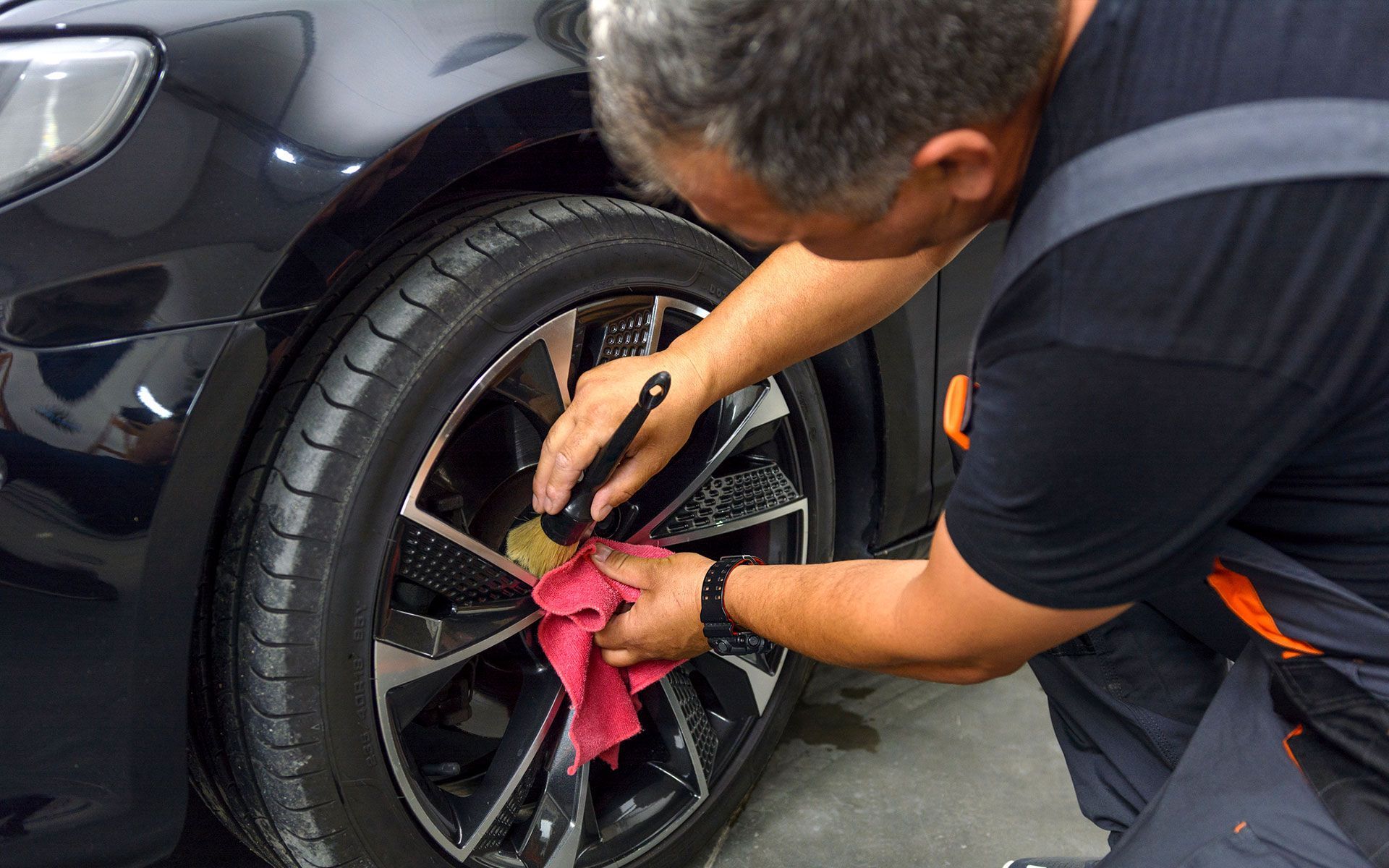 A man is cleaning a car wheel with a cloth.