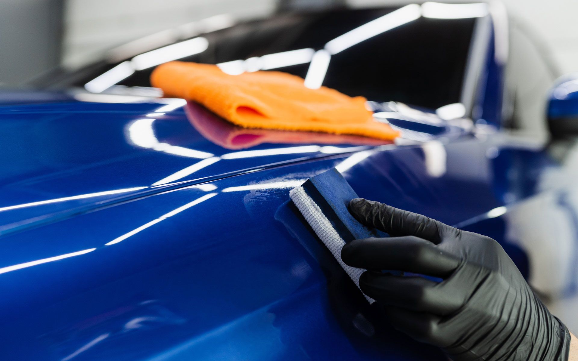 A person is polishing a blue car with a ceramic coating.