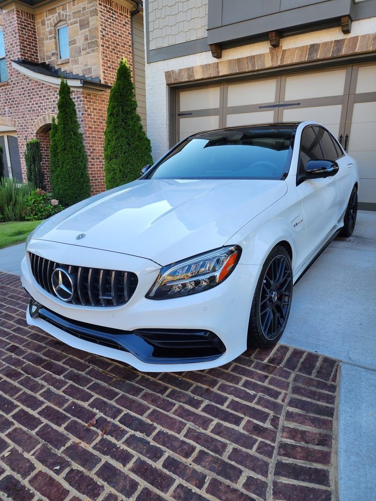 A white mercedes benz c63 amg is parked in front of a brick driveway.