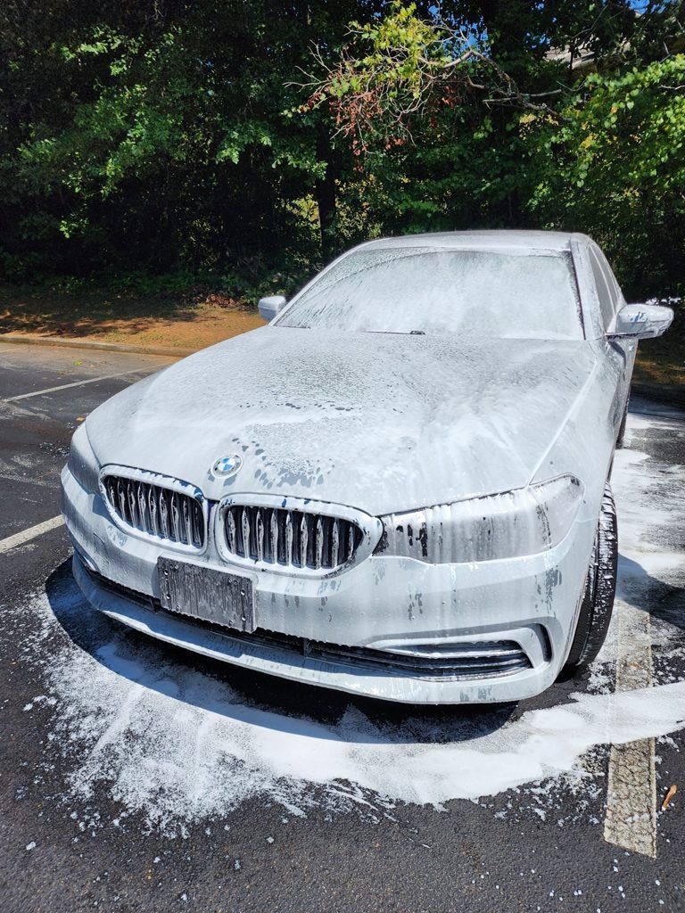 A white bmw is covered in foam in a parking lot.