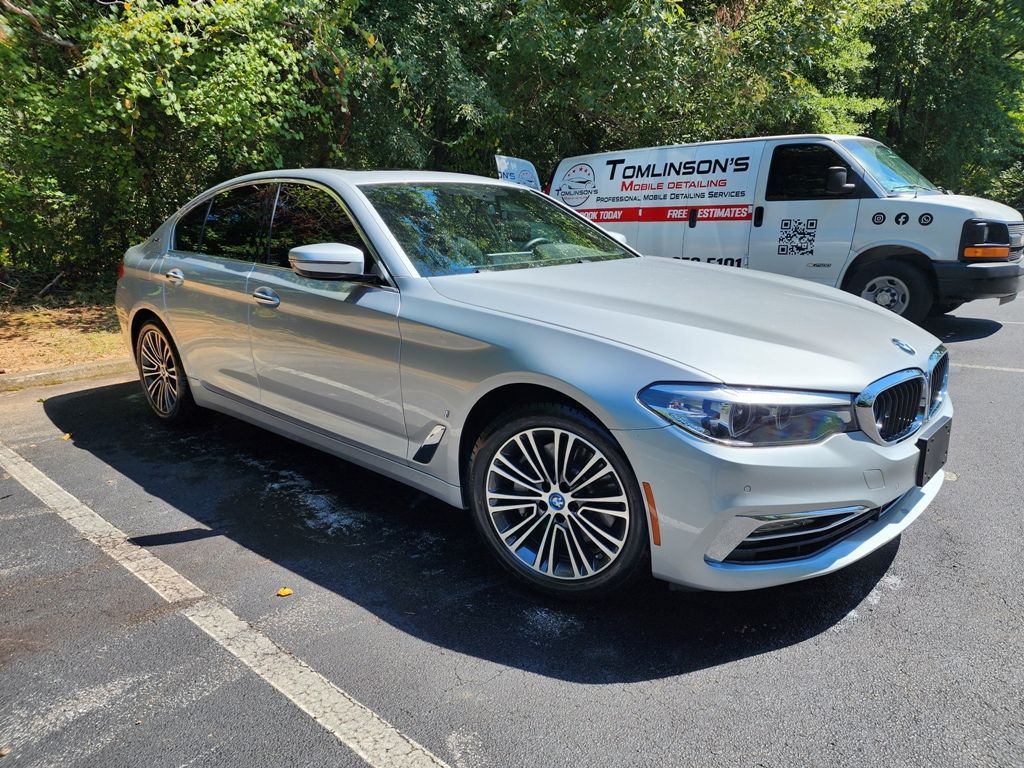 A silver bmw 5 series is parked in a parking lot next to a van.