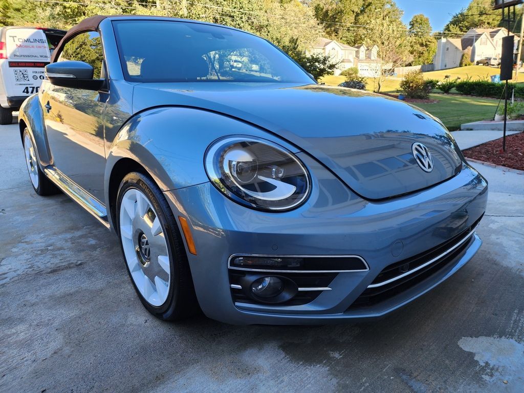 A volkswagen beetle convertible is parked in a driveway.