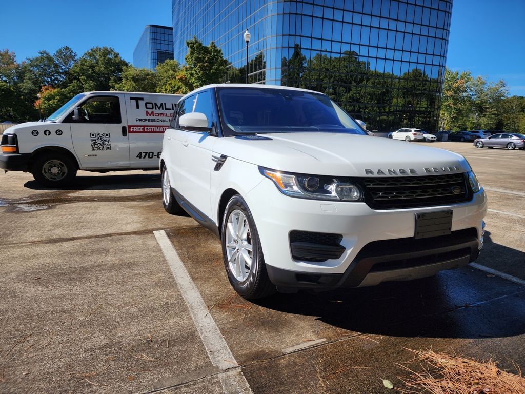 A white range rover sport is parked in a parking lot next to a tow truck.