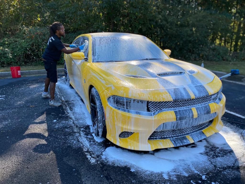 A woman is washing a yellow dodge charger with foam.