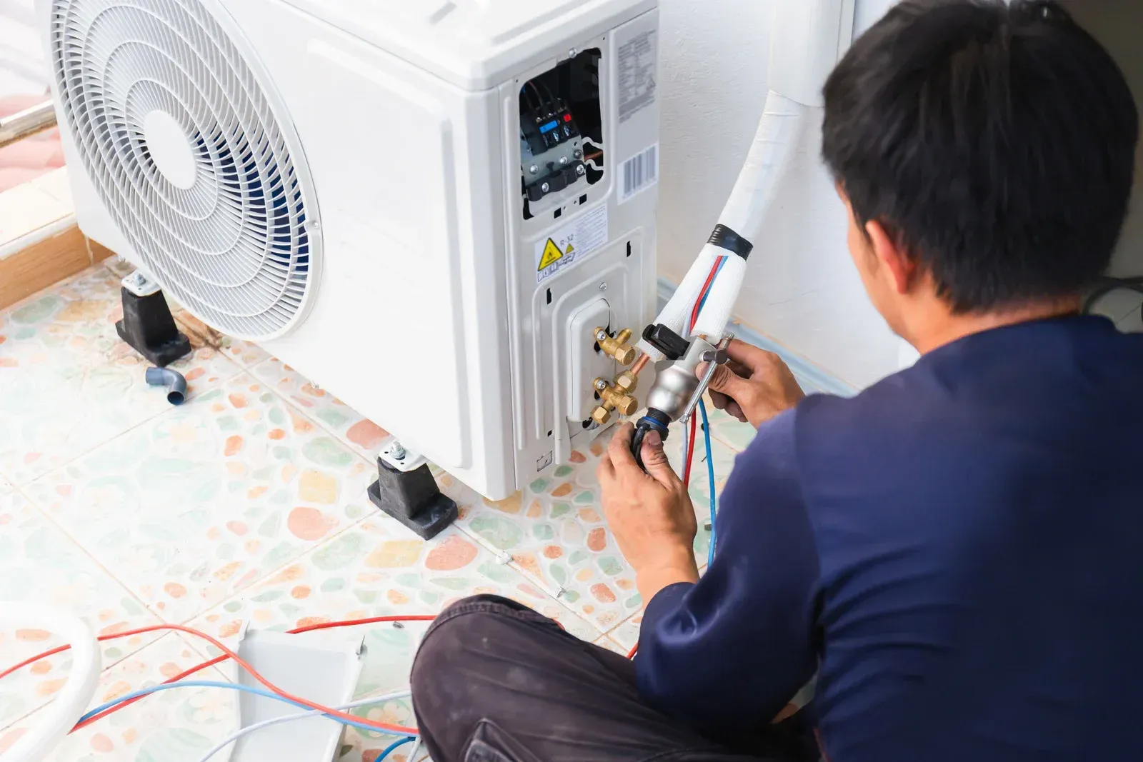 HVAC technician working on an air conditioning unit outside, connecting wires and pipes.