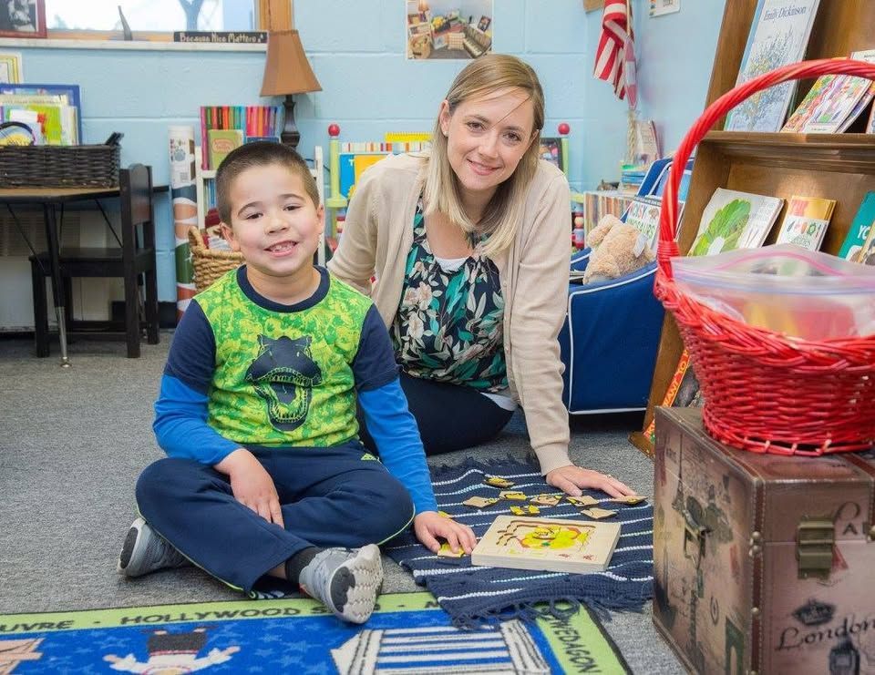 A woman and a boy are sitting on the floor in a classroom.