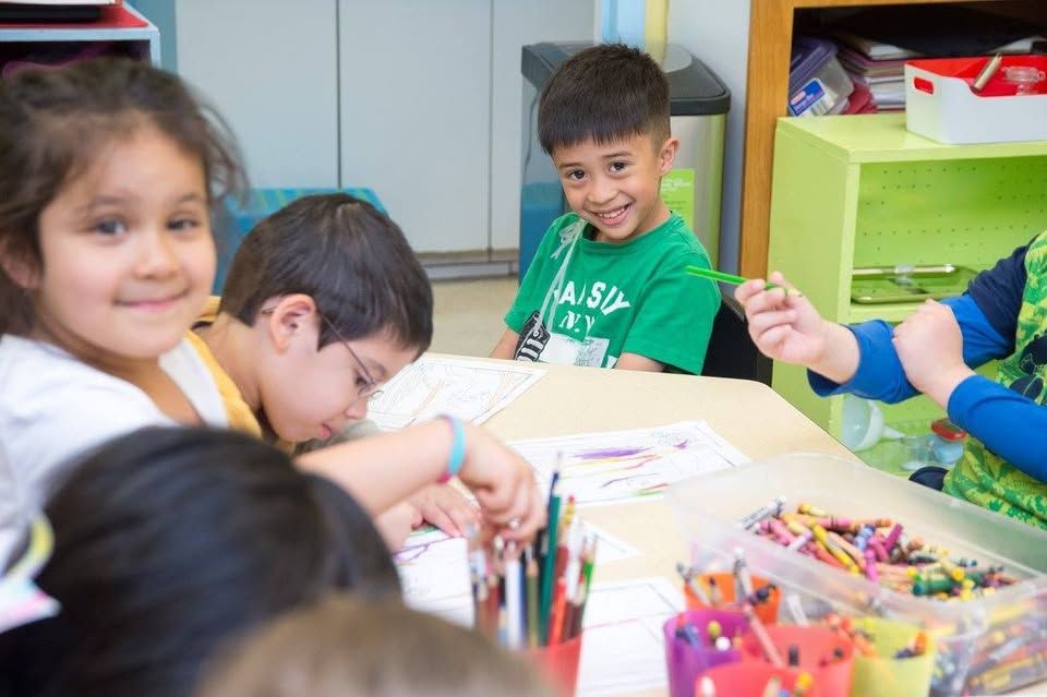 A group of children are sitting at a table in a classroom.