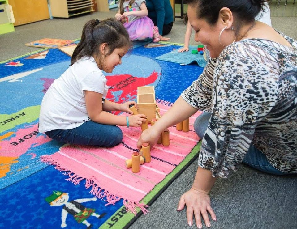 A woman and a little girl are playing with wooden blocks on the floor.