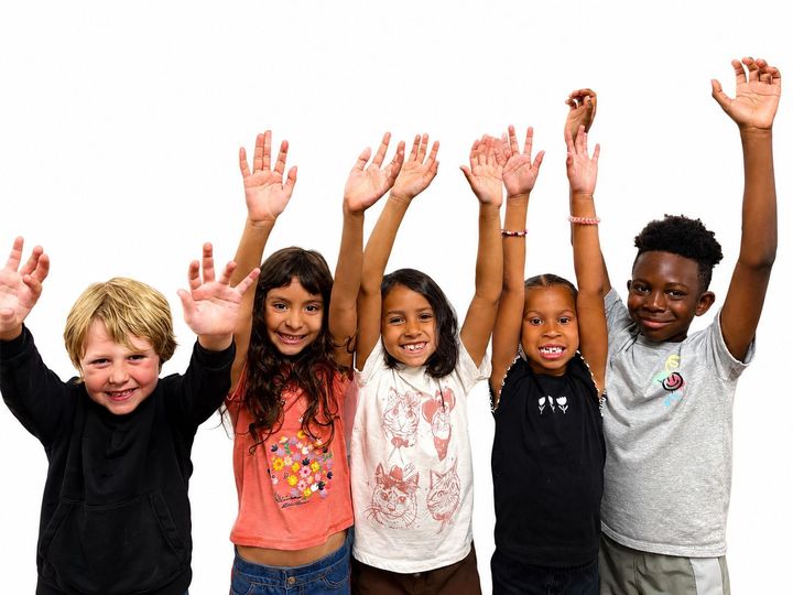 A group of children with backpacks are raising their hands in the air.