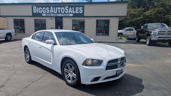 White Dodge Charger parked in front of Biggs Auto Sales building on a sunny day.