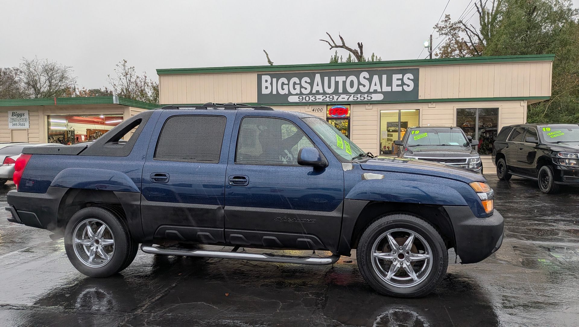 Blue Chevrolet Avalanche truck parked outside Bigos Auto Sales. Chrome wheels and running boards.