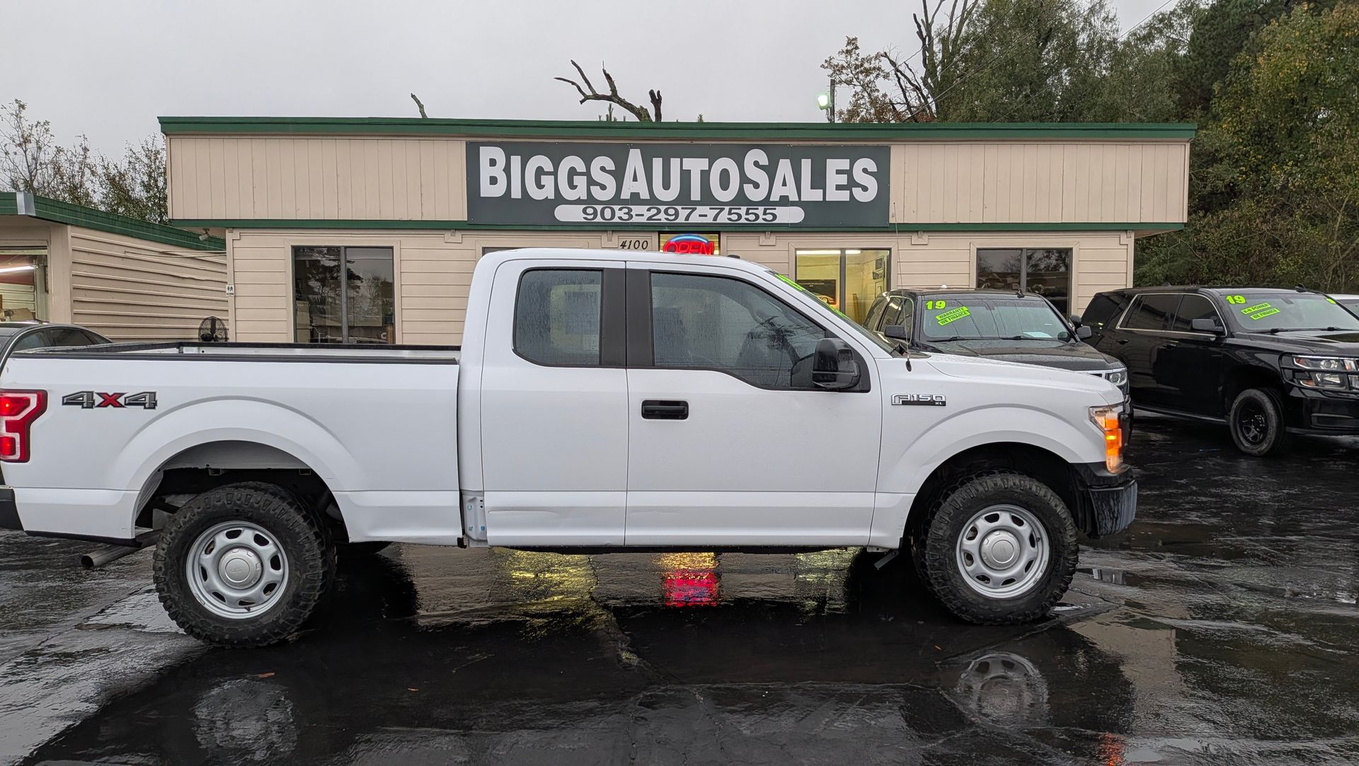 White Ford F-150 truck parked in front of Biggs Auto Sales; wet pavement.