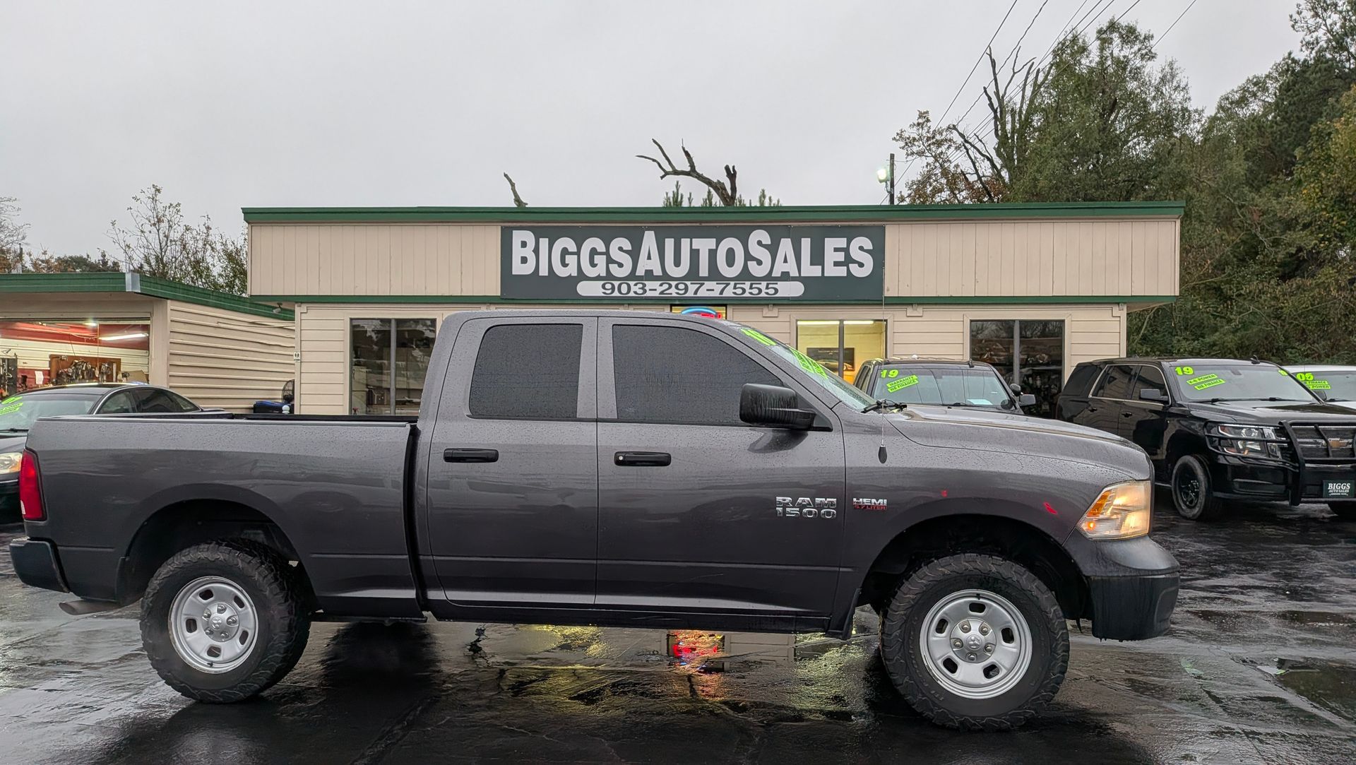 Gray Ram pickup truck parked in front of Biggs Auto Sales building on a rainy day.