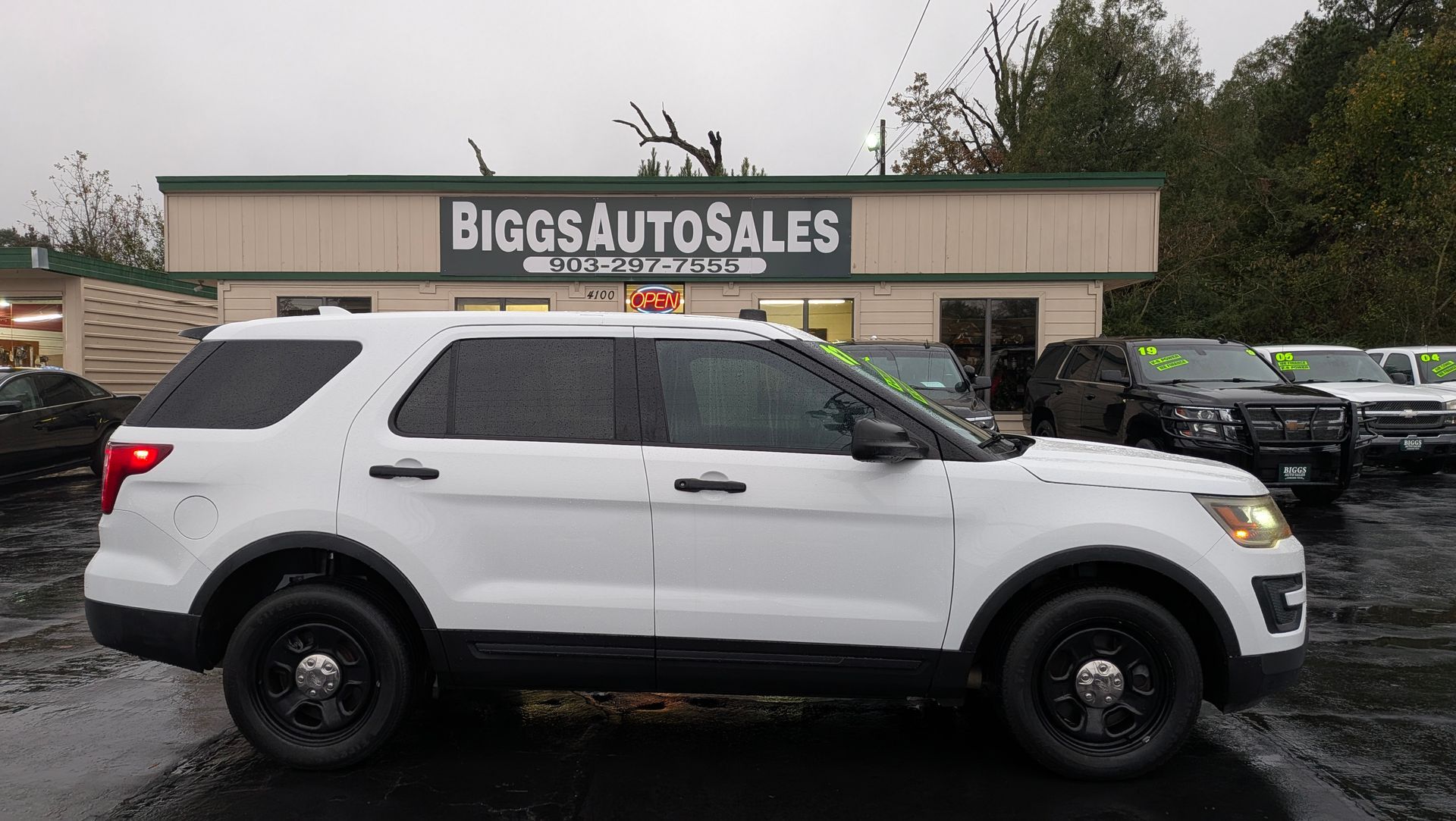 White Ford Explorer police SUV at Biggs Auto Sales, on a rainy day.