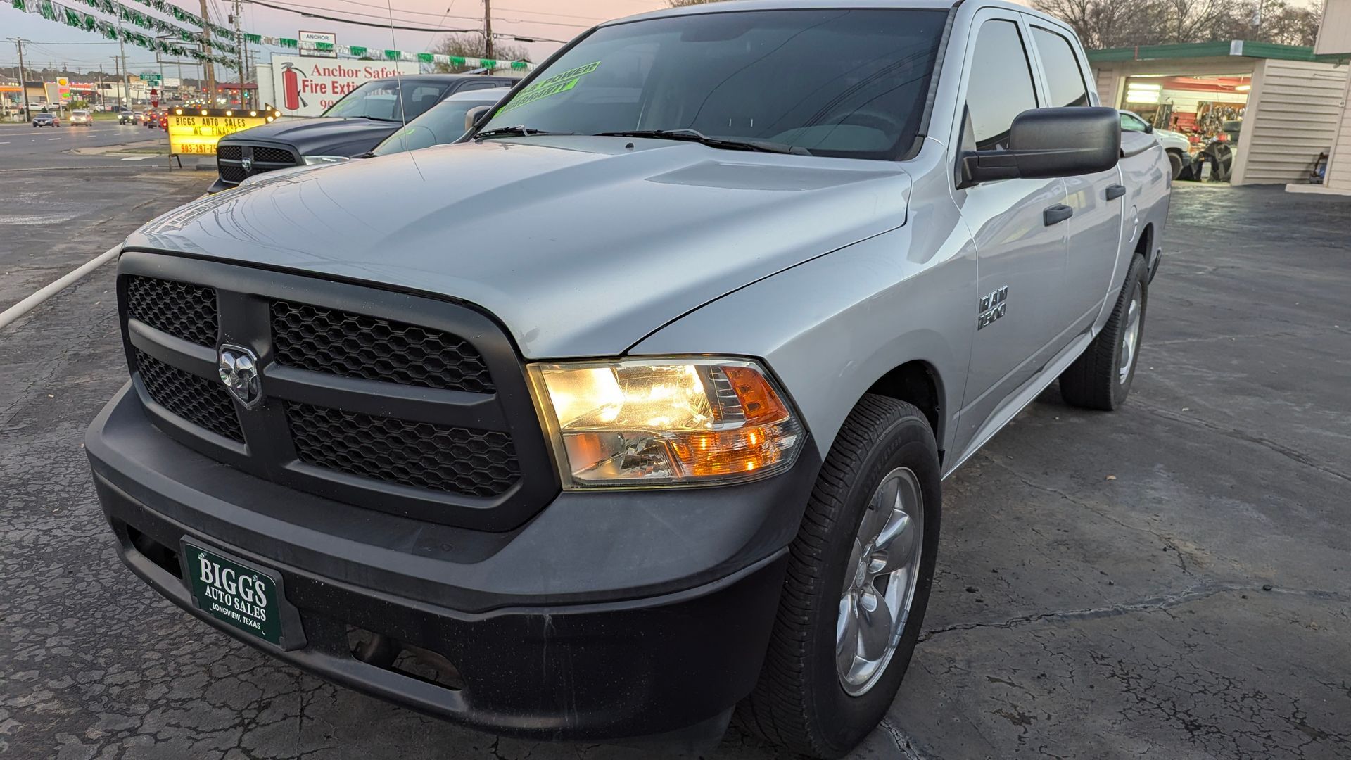 Silver Dodge Ram truck parked on a lot. Black grill, headlights on.