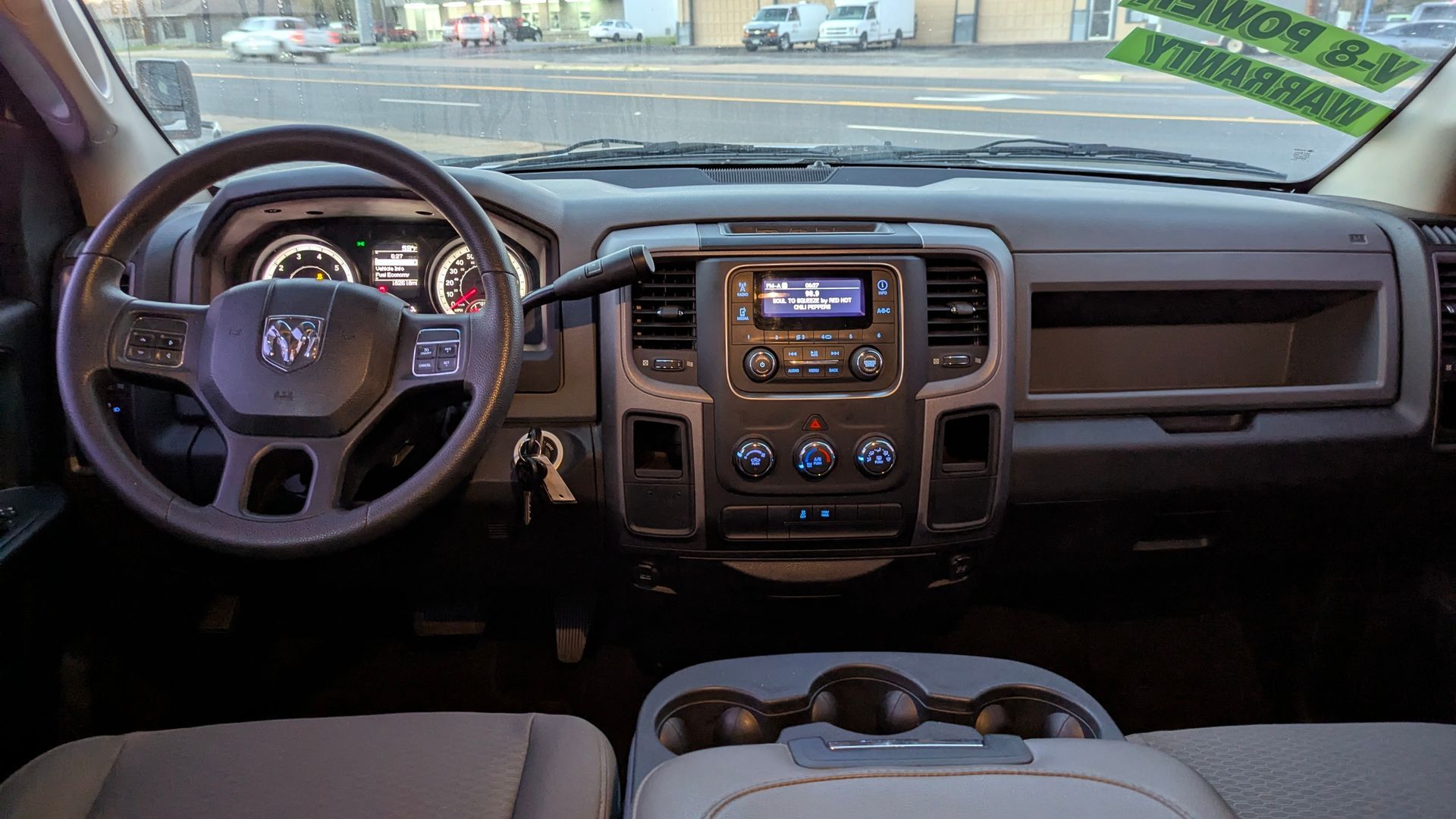 Interior of a truck: steering wheel, dashboard with radio, climate controls, and cup holders. Beige and gray colors.
