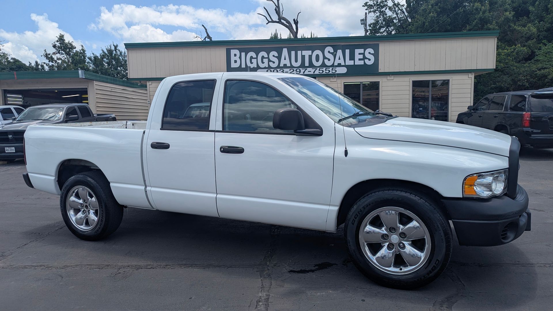 White Dodge Ram pickup truck parked in front of a car dealership.