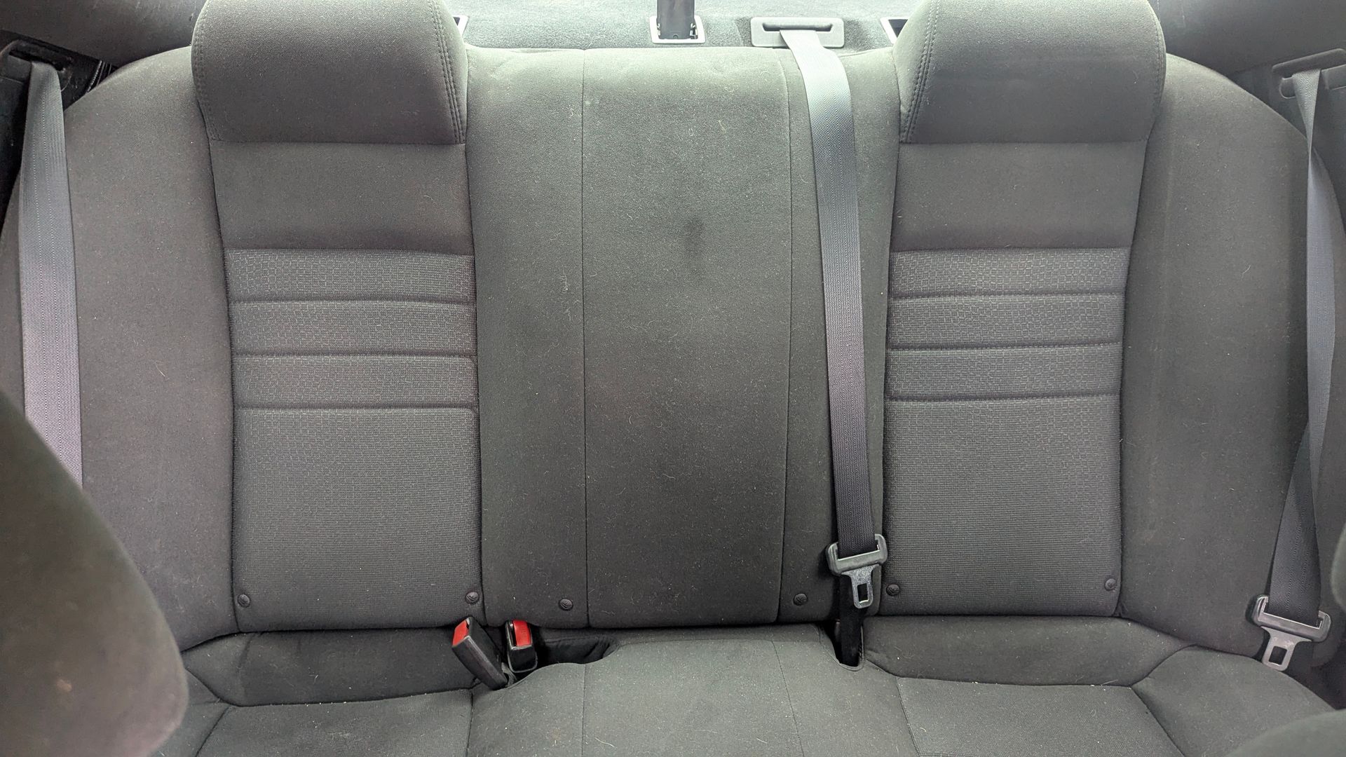 Gray car back seat with headrests and seatbelts.